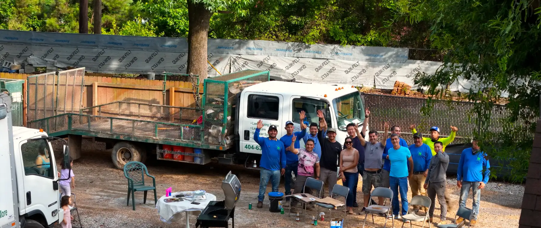 The whole ALS crew waving from the yard at an end-of-season cookout, trucks and trailers behind them
